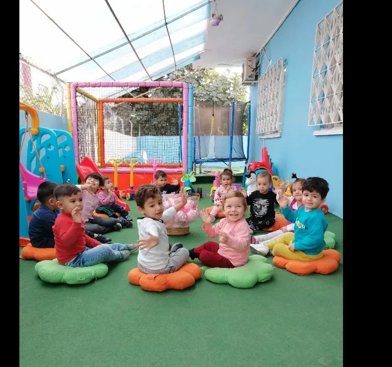 Geniş kapalı bahçemizde grup etkinliği — çocuklar çiçek minderlerde
